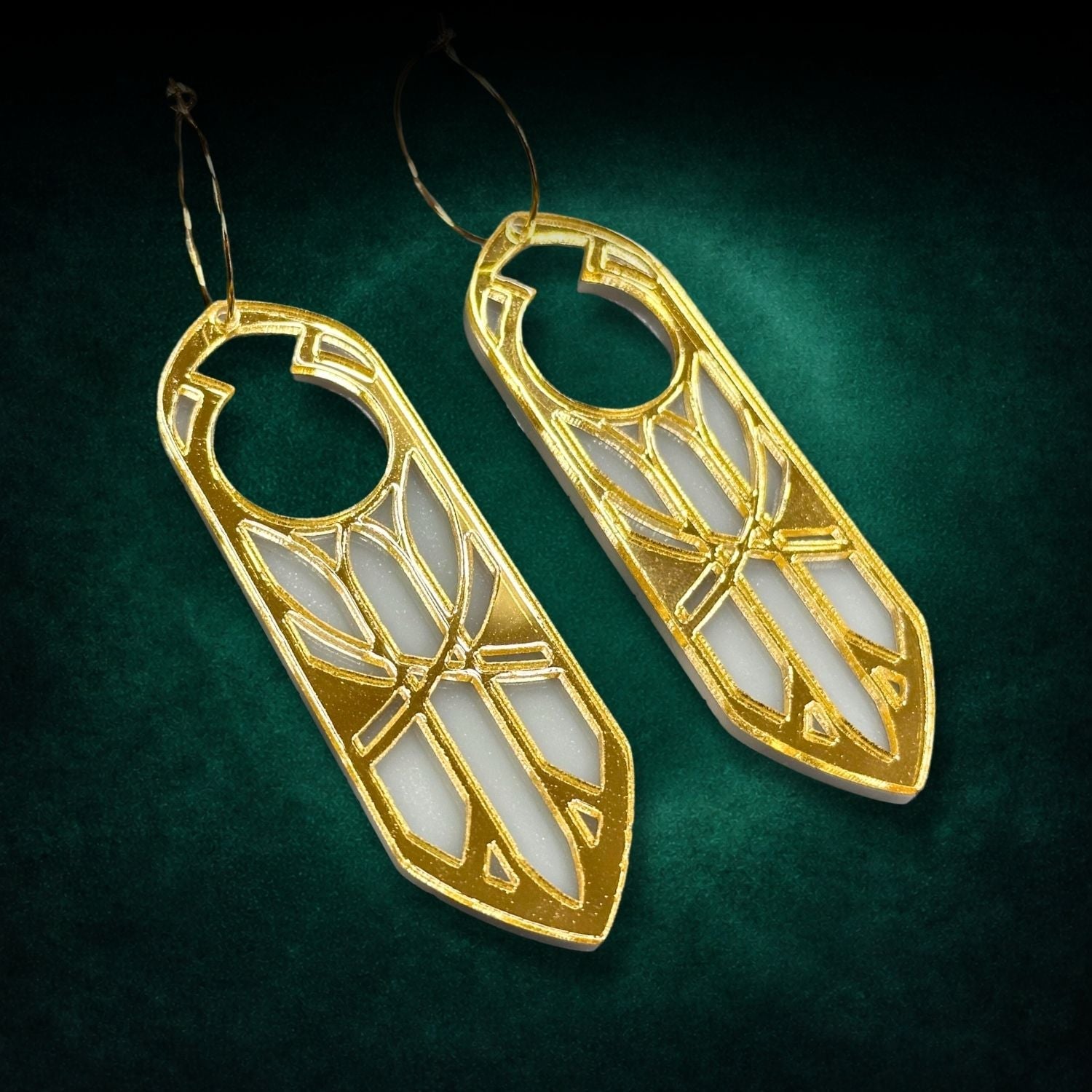 Gold and white geometric earrings on a green background