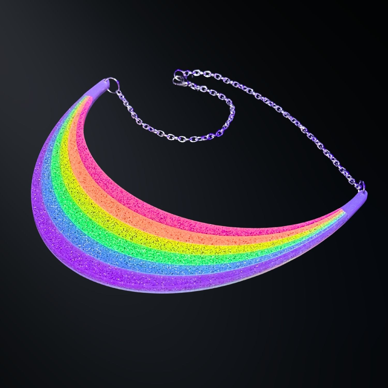 Full Spectrum Rebel Arc Statement Necklace in glitter rainbow acrylic with silver chain on a dark gradient background.