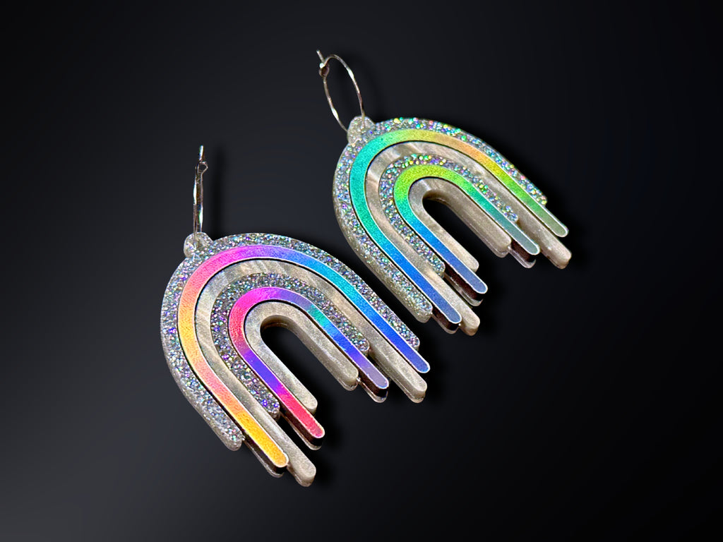 Disco Prism silver holographic drip earrings with shifting rainbow finishes displayed on a black background.