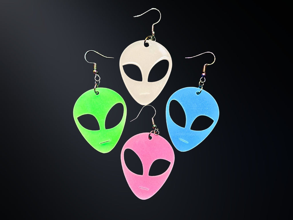 Glow in the Dark alien head earrings in neon green, blue, pink, and white acrylic on dark background.