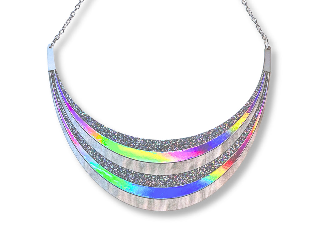 Close-up of Disco Prism arc statement necklace showing silver chain, clasp, holographic glitter, metallic silver, and iridescent rainbow layers.
