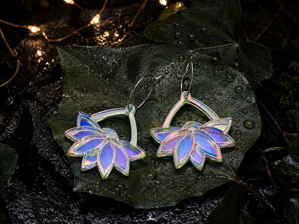Iridescent lotus hoop earrings displayed on dark leaves with fairy lights