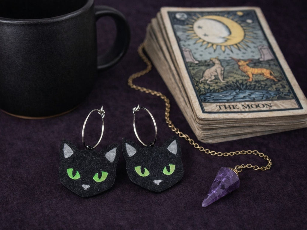 Black cat statement earrings styled with tarot cards, crystal pendant, and dark witchy accessories