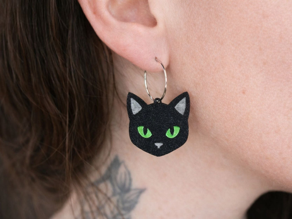 Model wearing black cat face acrylic hoop earrings with glowing green eyes