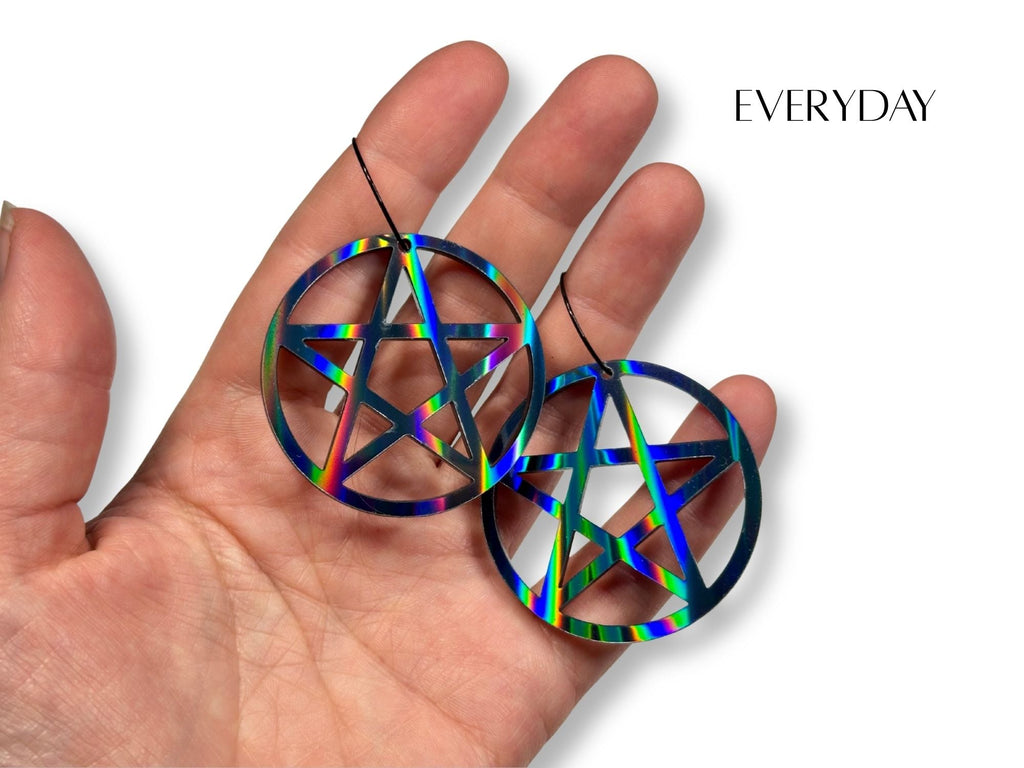 Everyday size black rainbow pentagram earrings shown in hand for scale reference