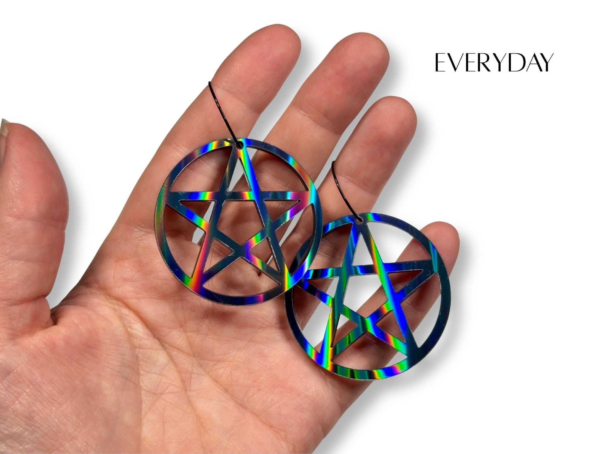 Everyday size black rainbow pentagram earrings shown in hand for scale reference