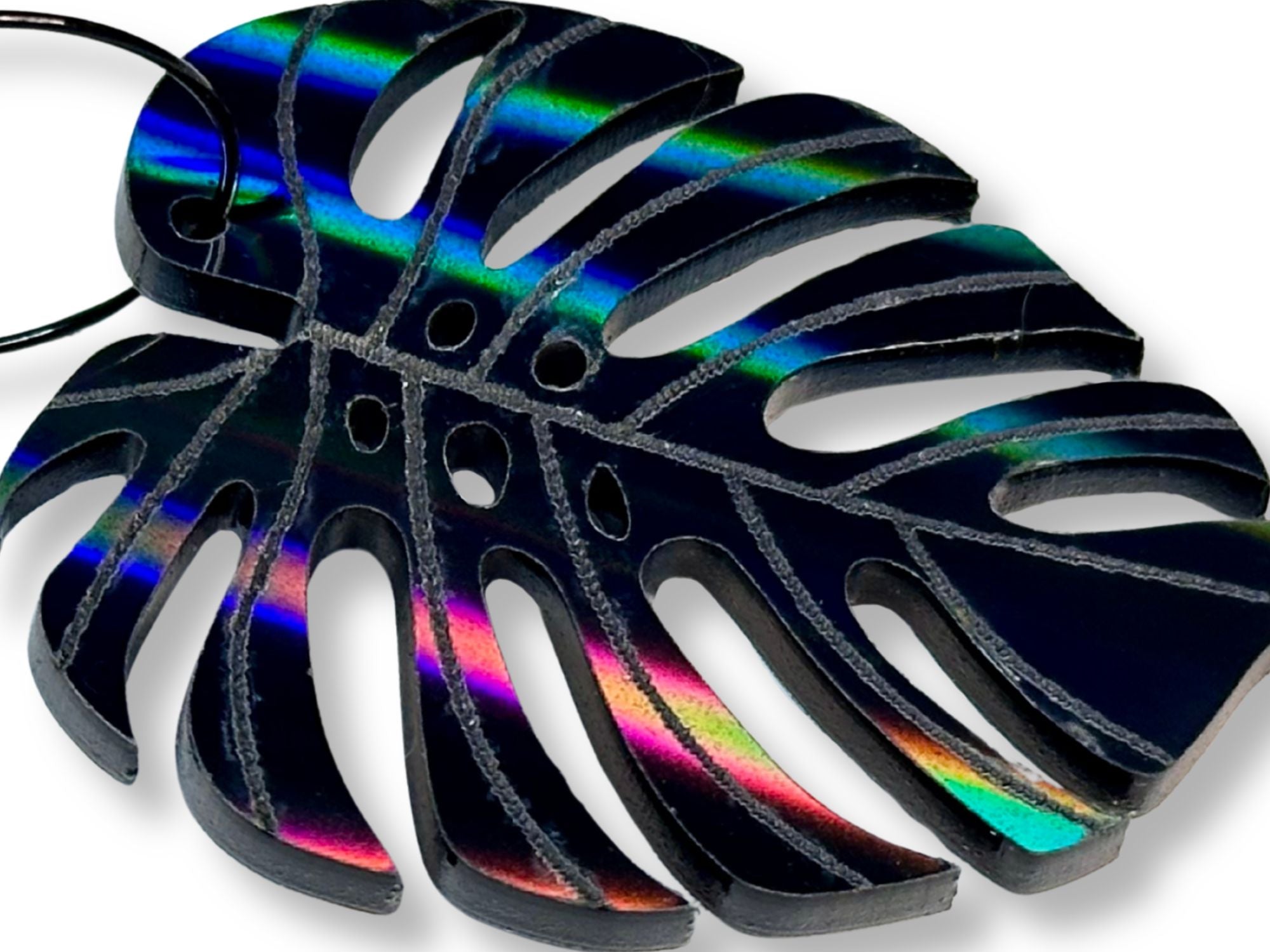 Close-up of a black rainbow iridescent monstera leaf acrylic earring showing holographic finish.