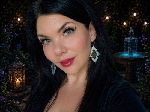Woman modeling silver gothic stained glass window earrings in candlelit garden setting