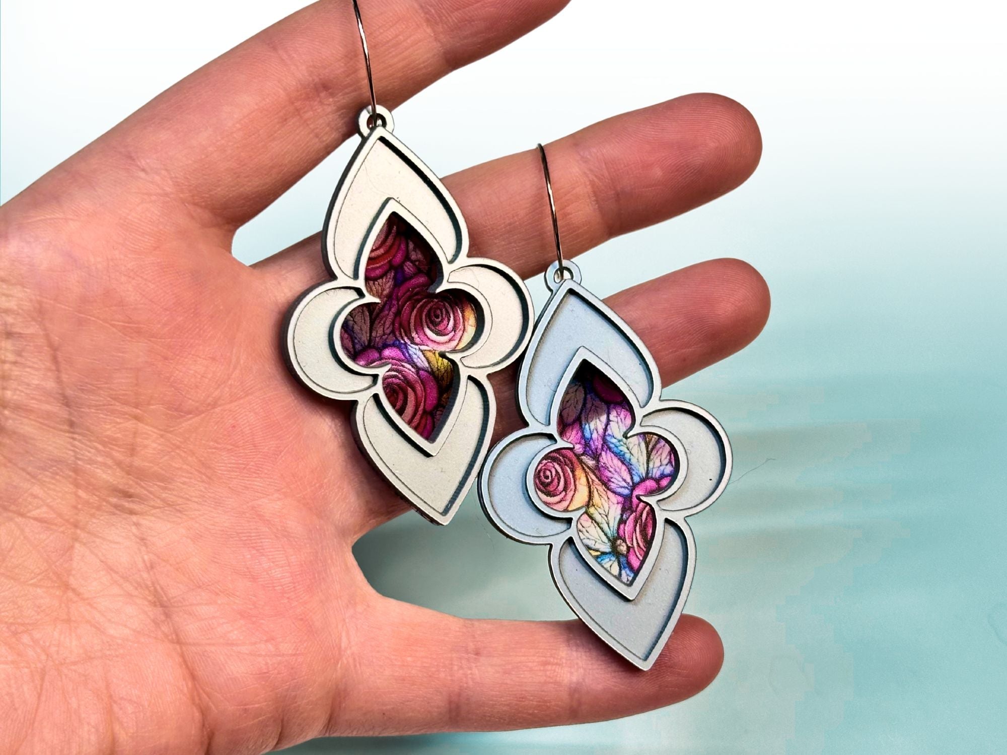 Hand holding metallic silver stained glass earrings with pink rose cathedral design