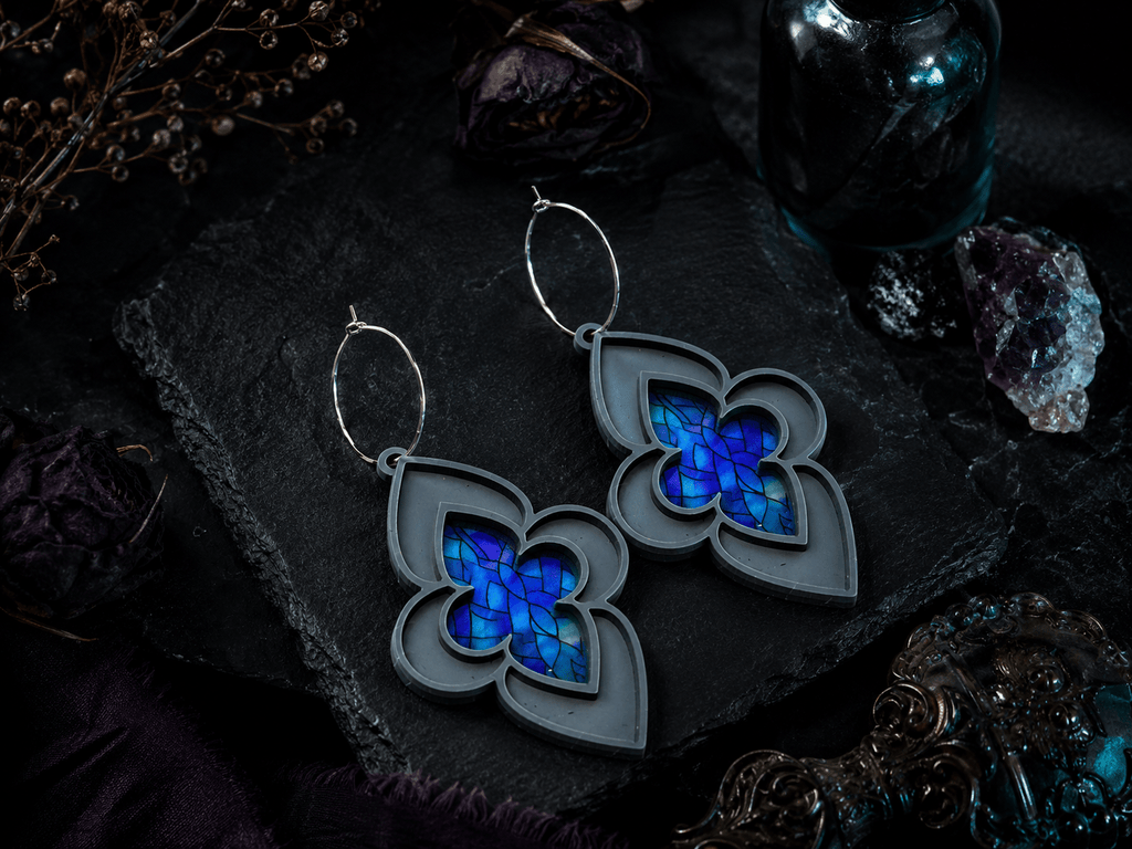 Blue stained glass cathedral earrings styled on dark gothic fabric with moody lighting