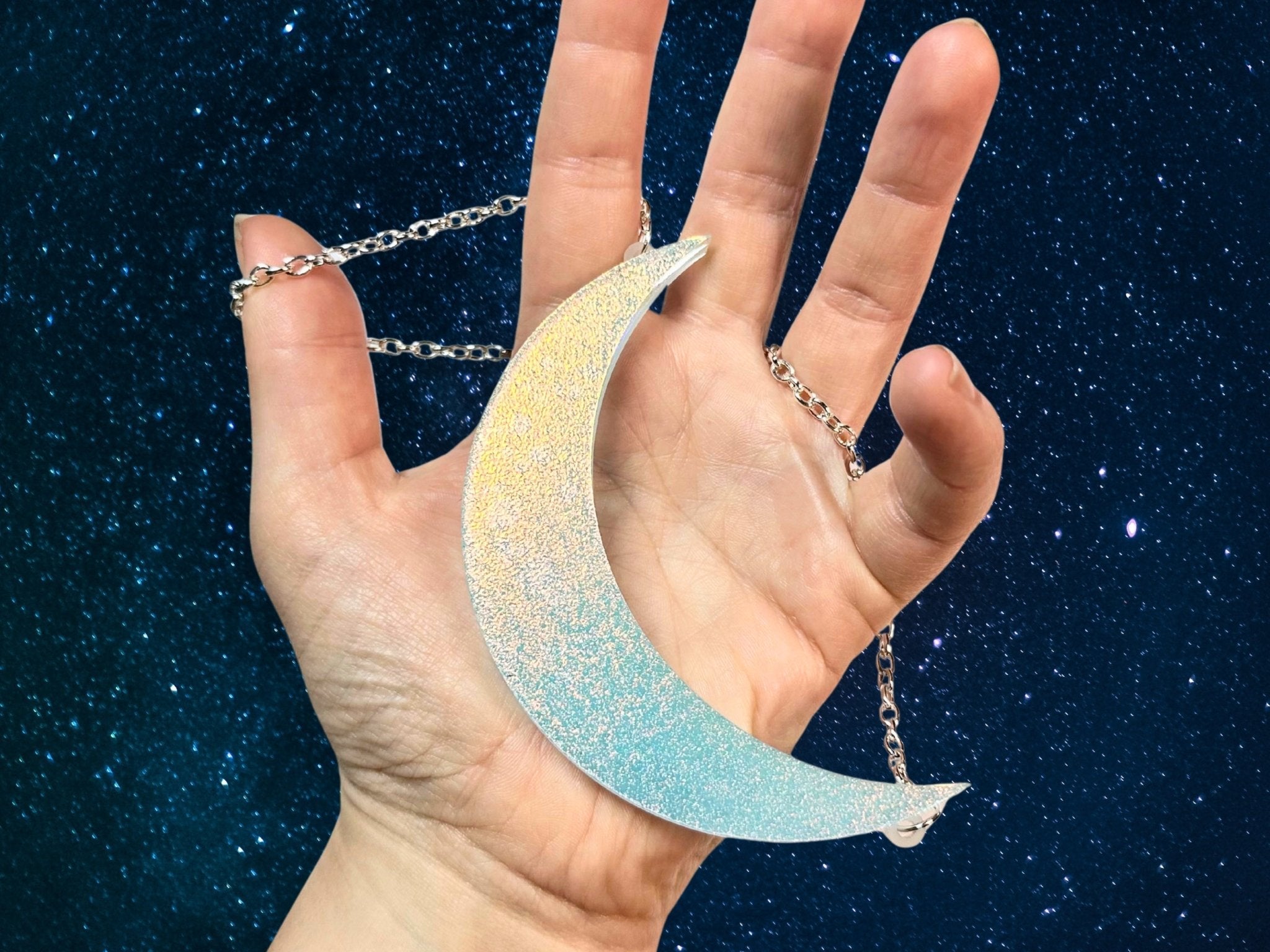Hand holding large iridescent crescent moon necklace showing statement size