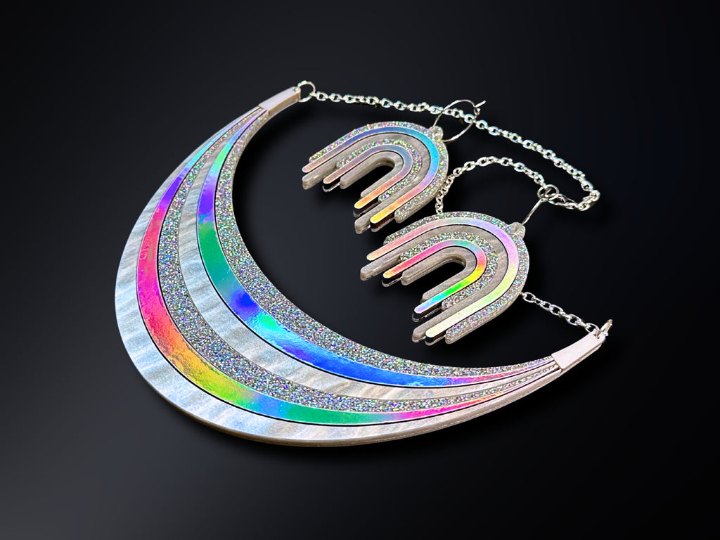 Full Spectrum Rebel Disco Prism jewelry set featuring a silver holographic arc statement necklace and matching rainbow drip earrings on a black background.