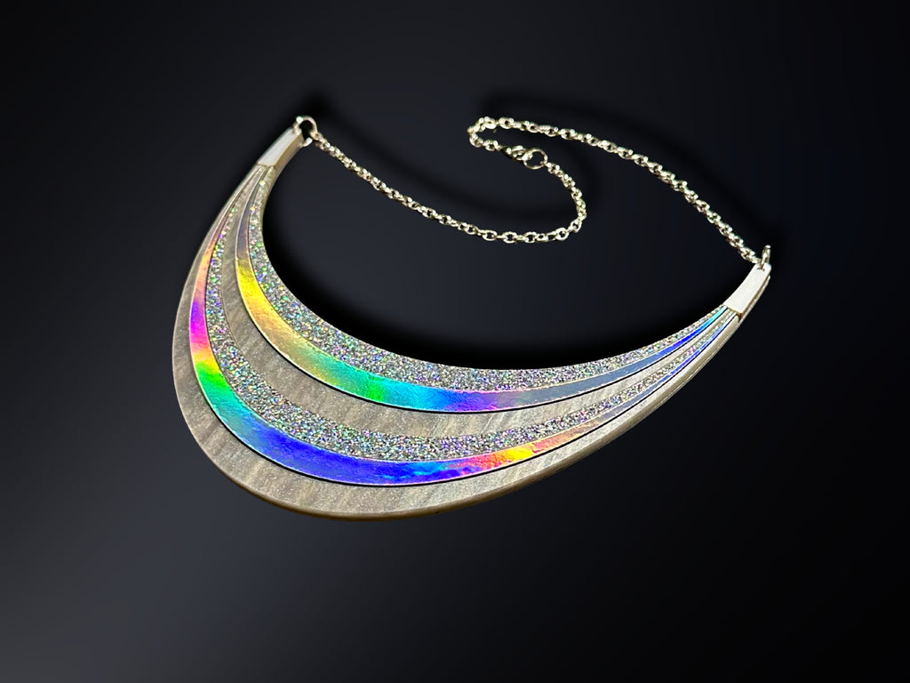 Disco Prism silver holographic arc statement necklace with layered rainbow and glitter details on a black background.
