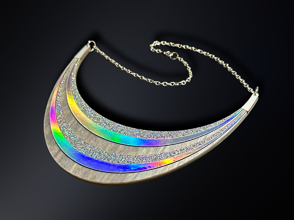 Disco Prism silver holographic arc statement necklace with layered glitter and color-shifting rainbow details on a black background.