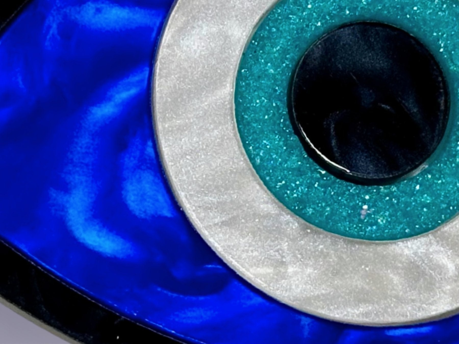 close up of evil eye necklace showing pearl acrylic detail layered construction and reflective surface with resin druzy crysta;