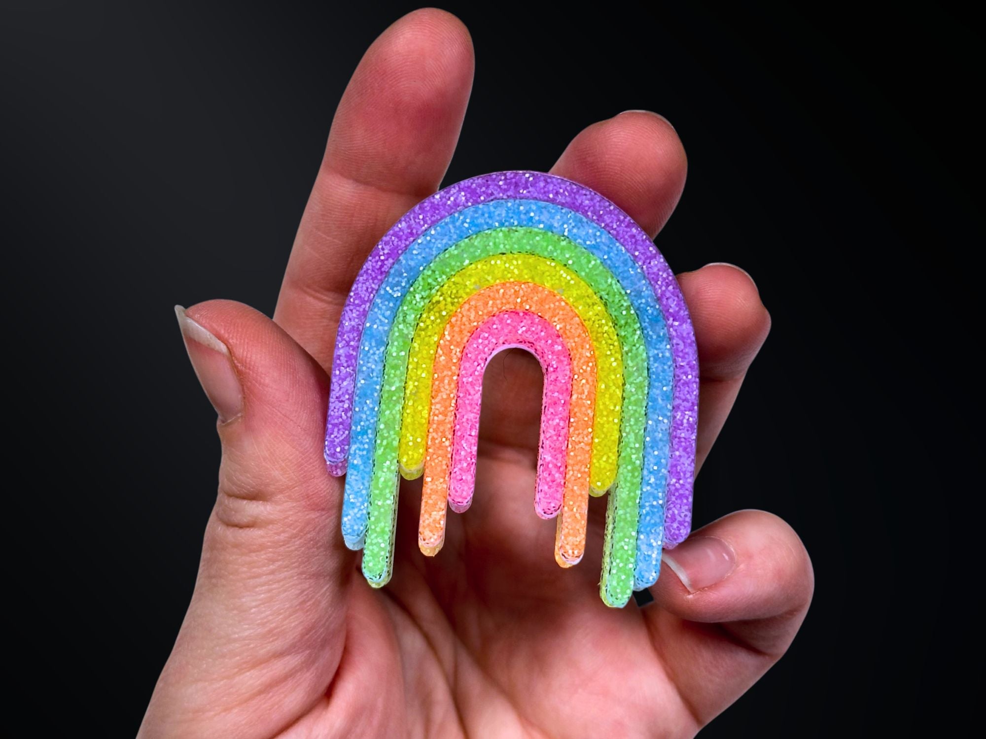 Hand holding Full Spectrum Rebel Rainbow Rave glitter acrylic drip brooch for scale reference.