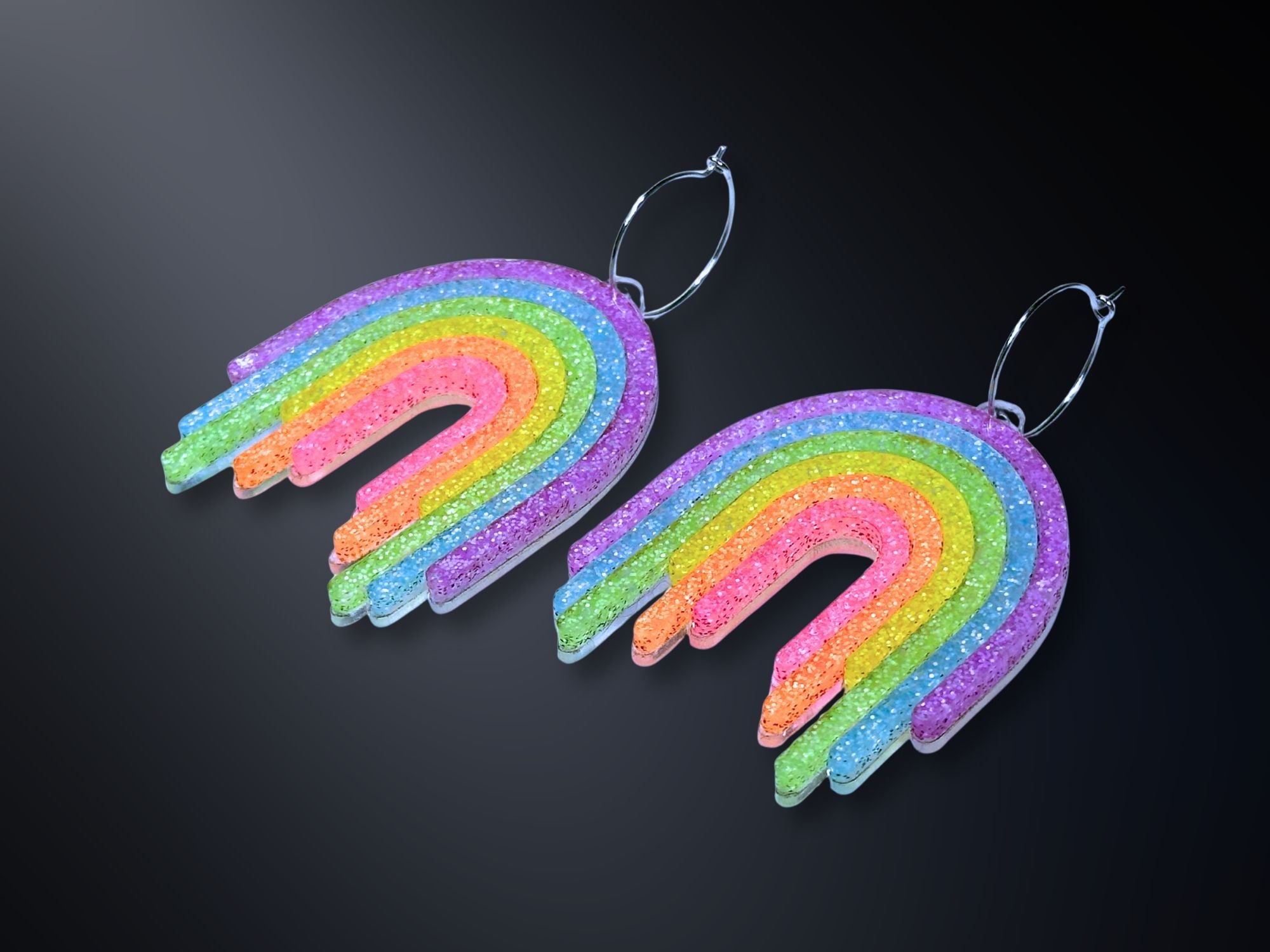 Full Spectrum Rebel Rainbow Rave statement earrings in glitter rainbow acrylic on dark gradient background.