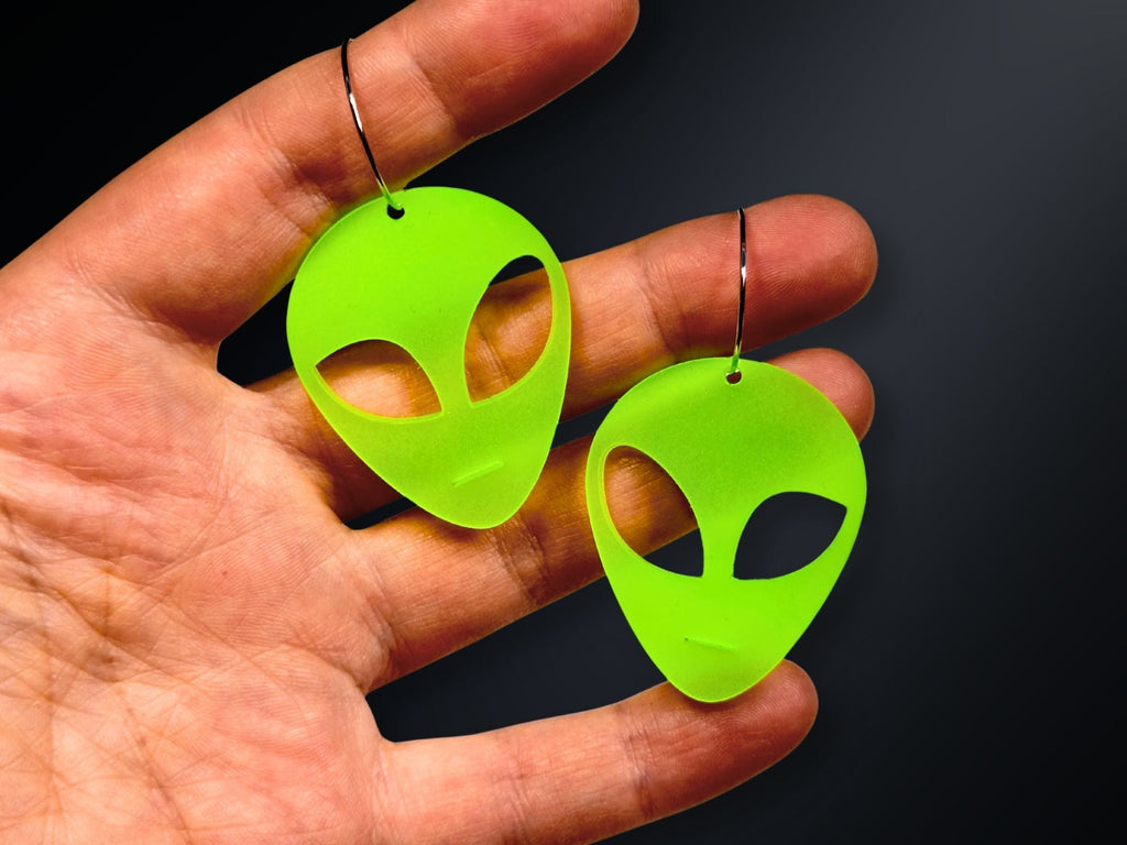 Hand holding glow in the dark neon green alien acrylic earrings for scale reference.