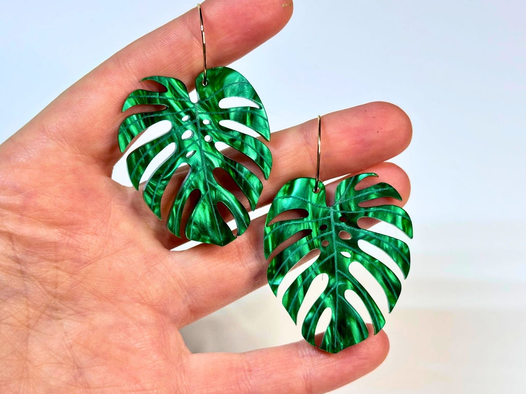 Monstera leaf statement earrings shown in hand for size reference.