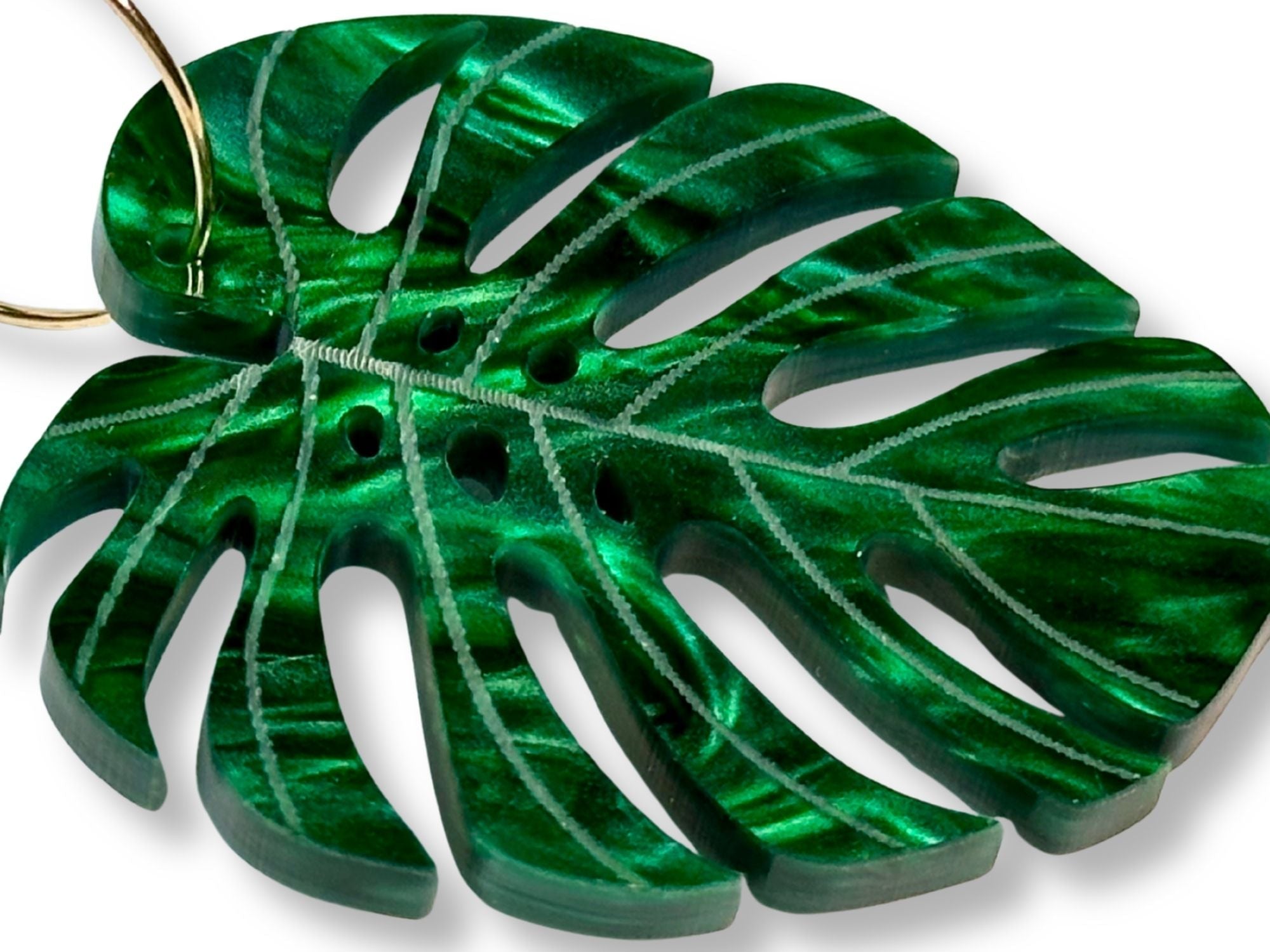 Close-up of engraved monstera leaf earring showing detailed vein engraving and pearlescent green acrylic.