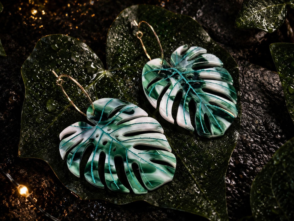 Ghost Variegata monstera leaf earrings photographed on rain-kissed tropical foliage, highlighting engraved veins and variegated green-and-white marbled acrylic.