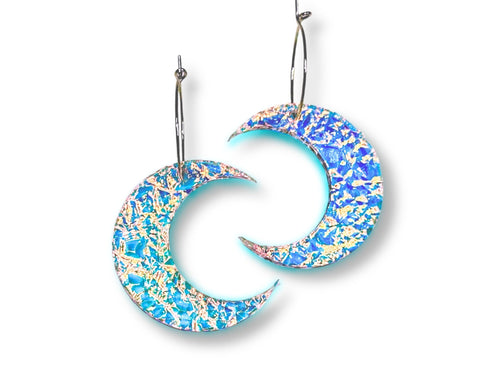 Textured iridescent crescent moon statement earrings with blue and rainbow reflective finish on white background.