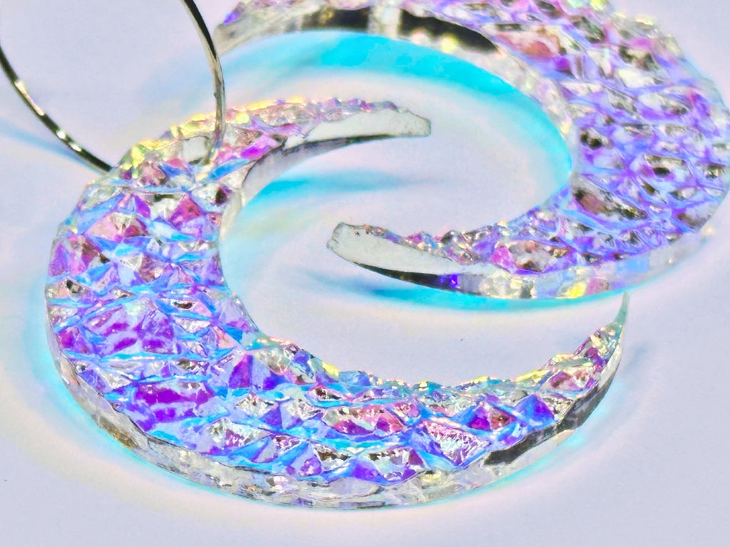 Close-up of textured iridescent crescent moon earrings showing rainbow reflective surface.