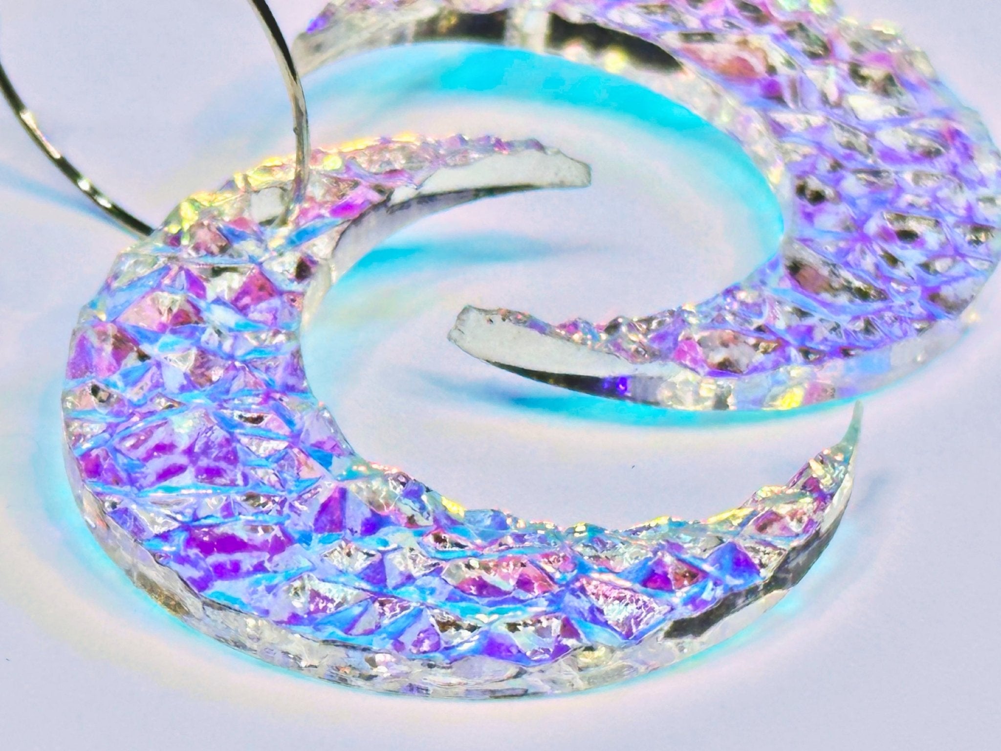 Close-up of textured iridescent crescent moon earrings showing rainbow reflective surface.