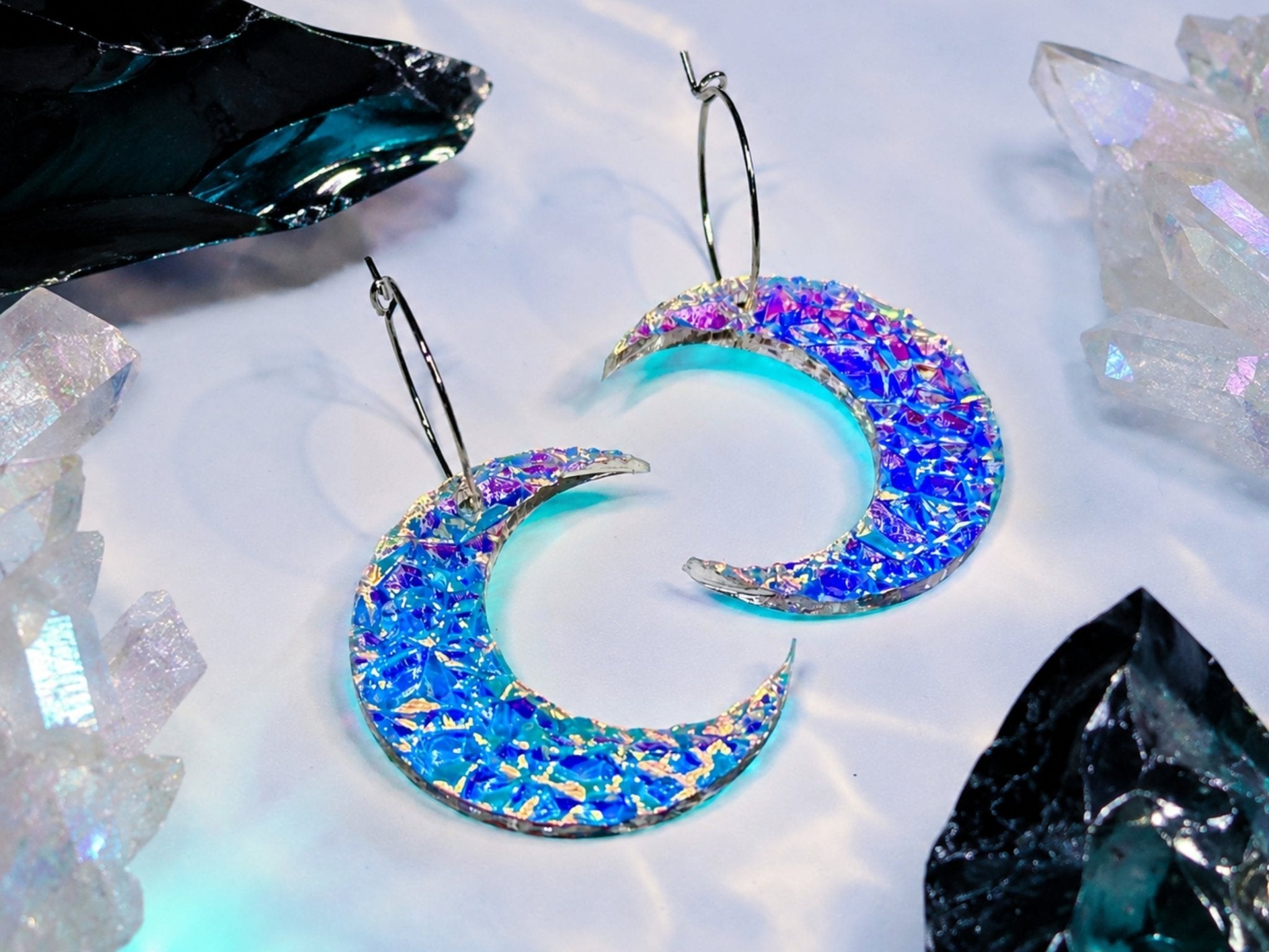Blue iridescent crescent moon statement earrings photographed with crystals and black stones.