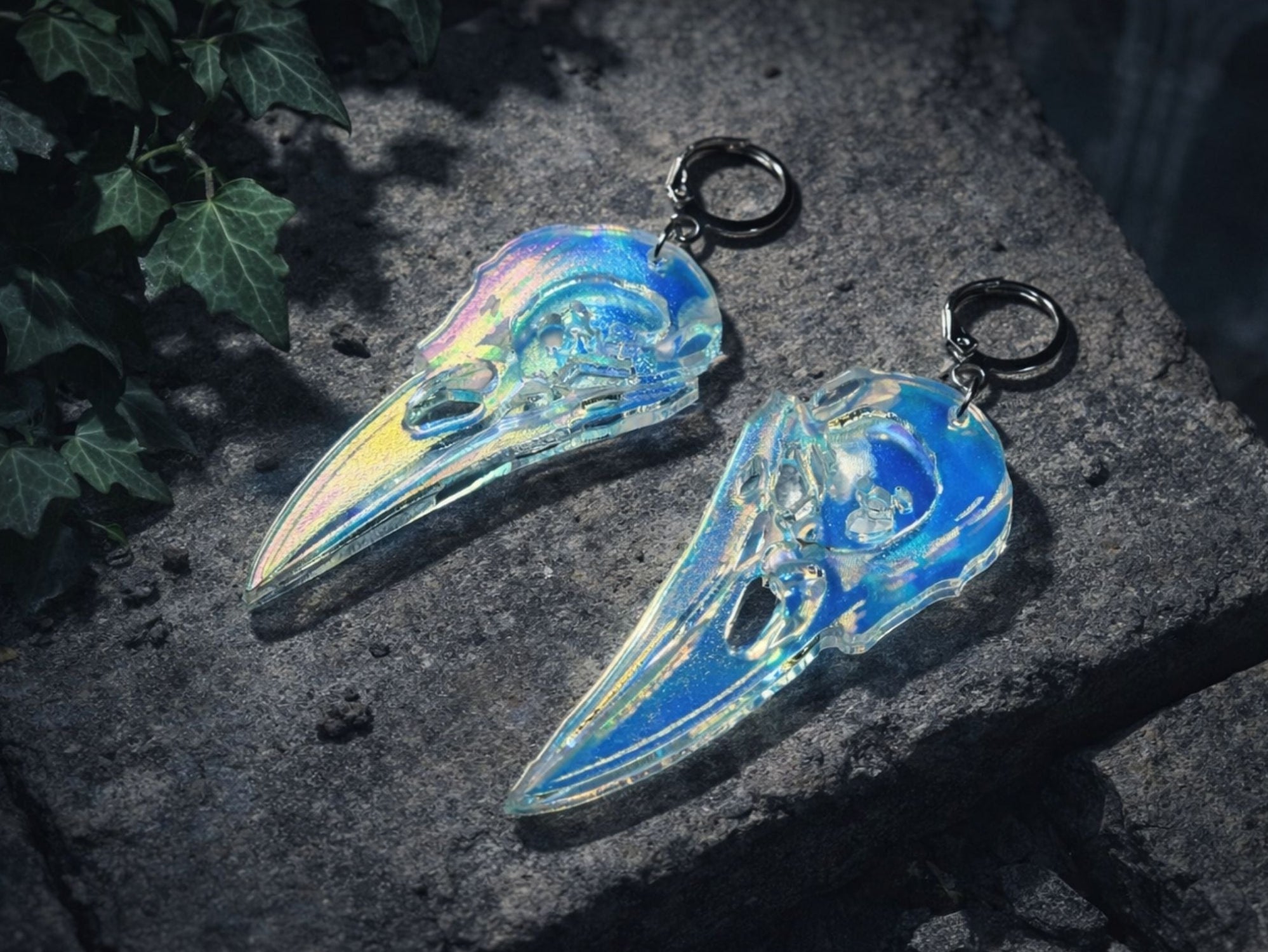Iridescent raven skull acrylic earrings photographed outdoors on dark stone surface.