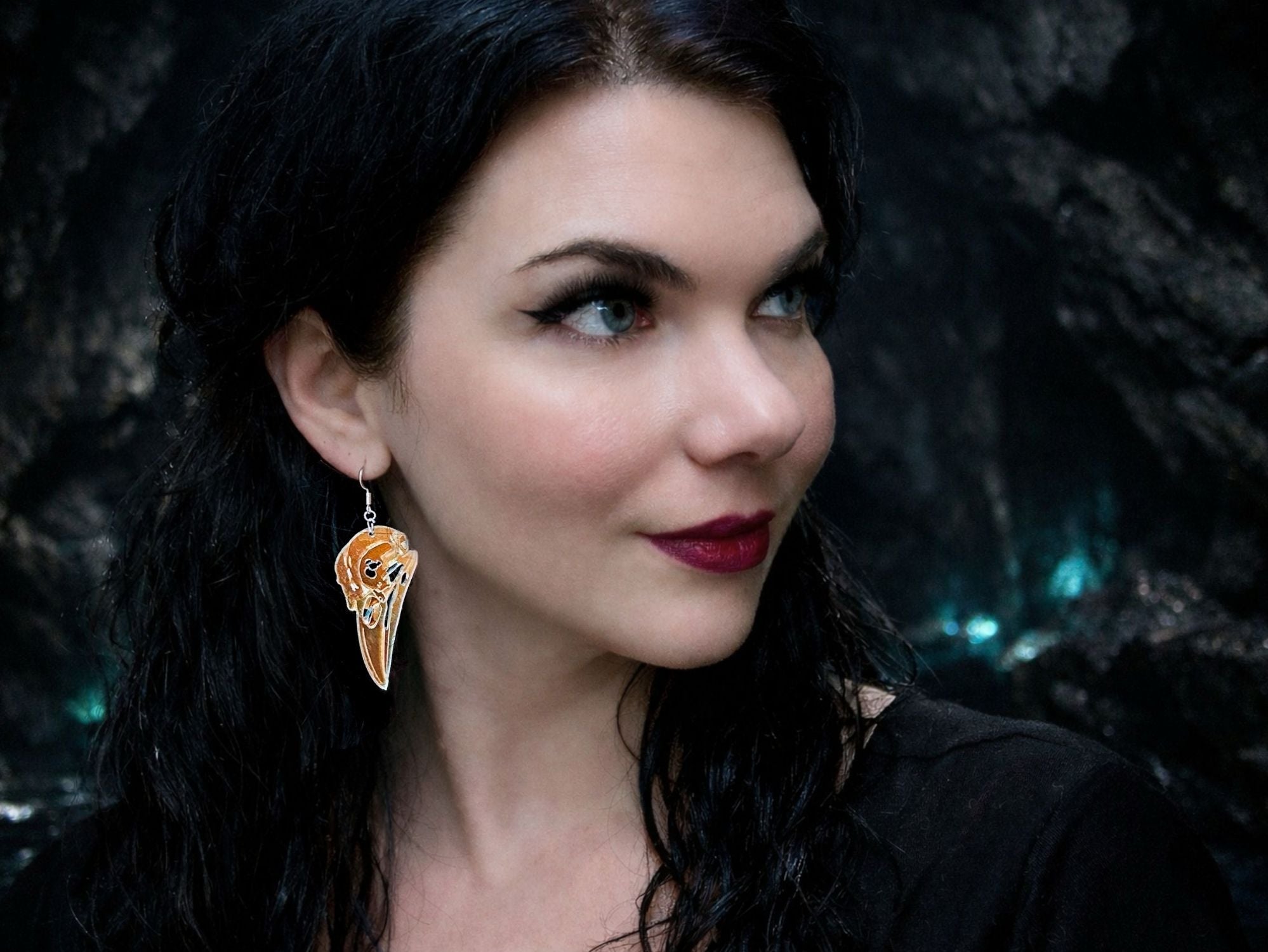 Model wearing iridescent raven skull earrings in translucent acrylic.