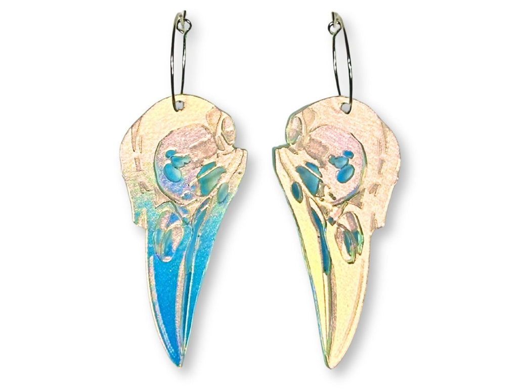 Raven skull statement earrings in iridescent transparent acrylic with silver hoop ear wires on white background.