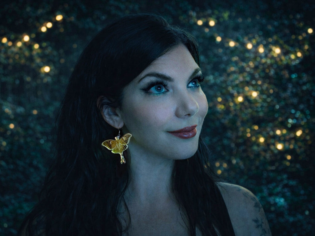 Woman wearing an iridescent Luna moth earring, showing the dramatic 60mm wingspan and statement scale when worn.