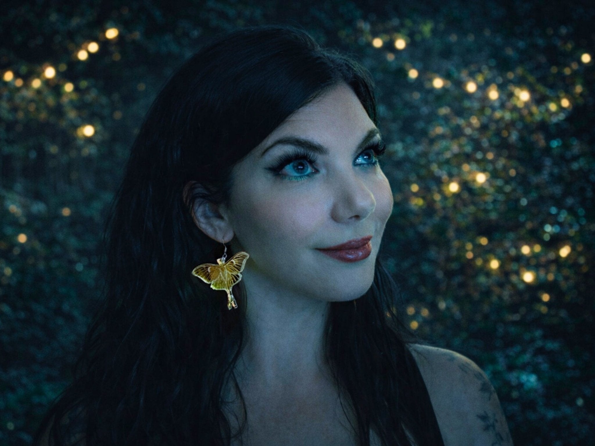 Woman wearing an iridescent Luna moth earring, showing the dramatic 60mm wingspan and statement scale when worn.