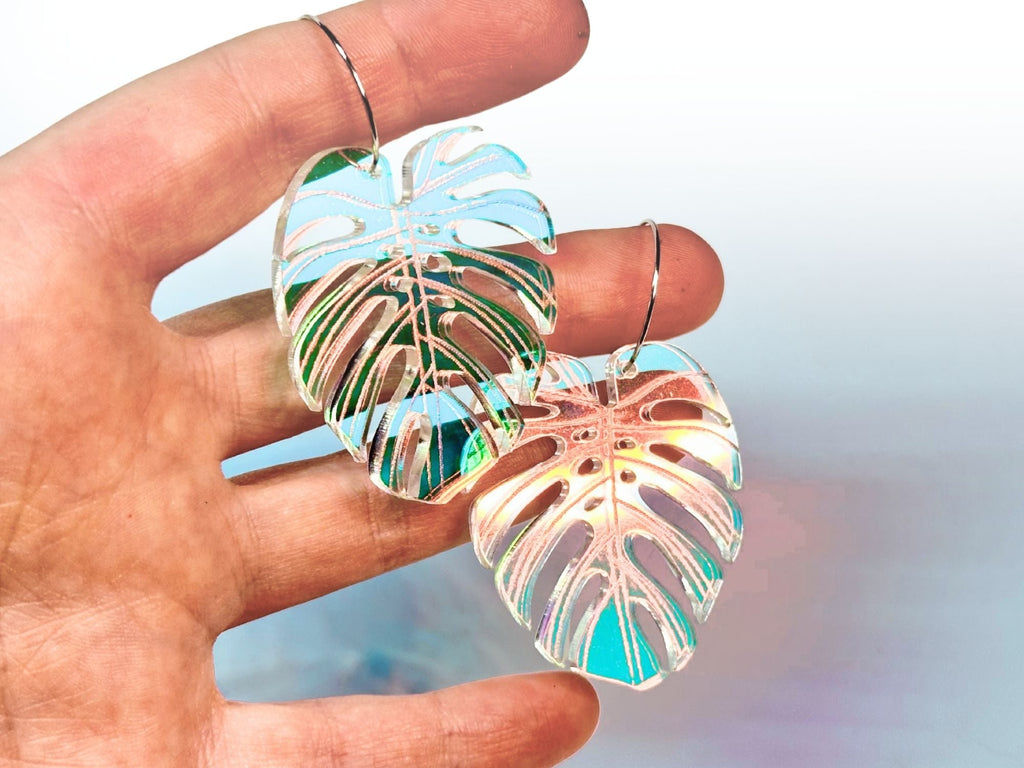 Hand holding oversized iridescent monstera leaf earrings to show their lightweight size and shimmering tropical finish.