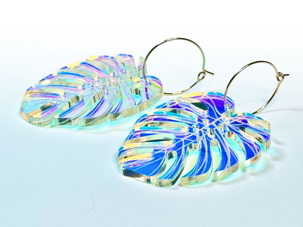 Pair of iridescent monstera leaf acrylic earrings showing engraved leaf veins and color-shifting tropical shimmer.