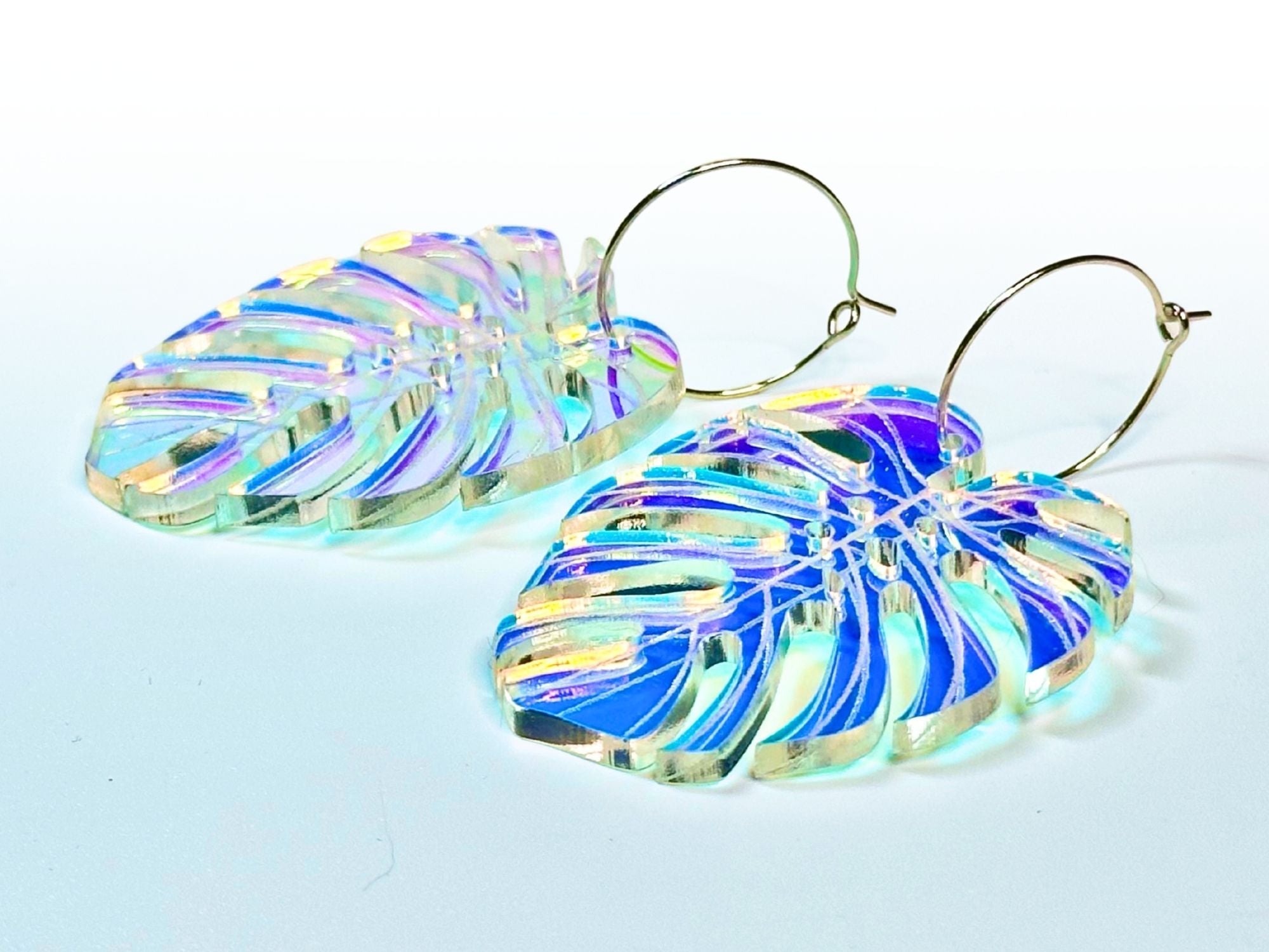 Pair of iridescent monstera leaf acrylic earrings showing engraved leaf veins and color-shifting tropical shimmer.