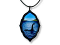 Loch Ness Monster acrylic pendant hanging from a black faux leather cord on a white background.