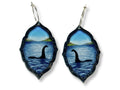 Loch Ness monster statement earrings in layered acrylic with blue lake scene and silver hoop ear wires on white background.
