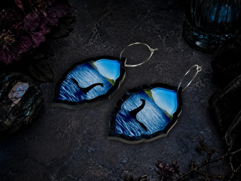 Acrylic Nessie earrings with blue water landscape photographed on dark moody background.