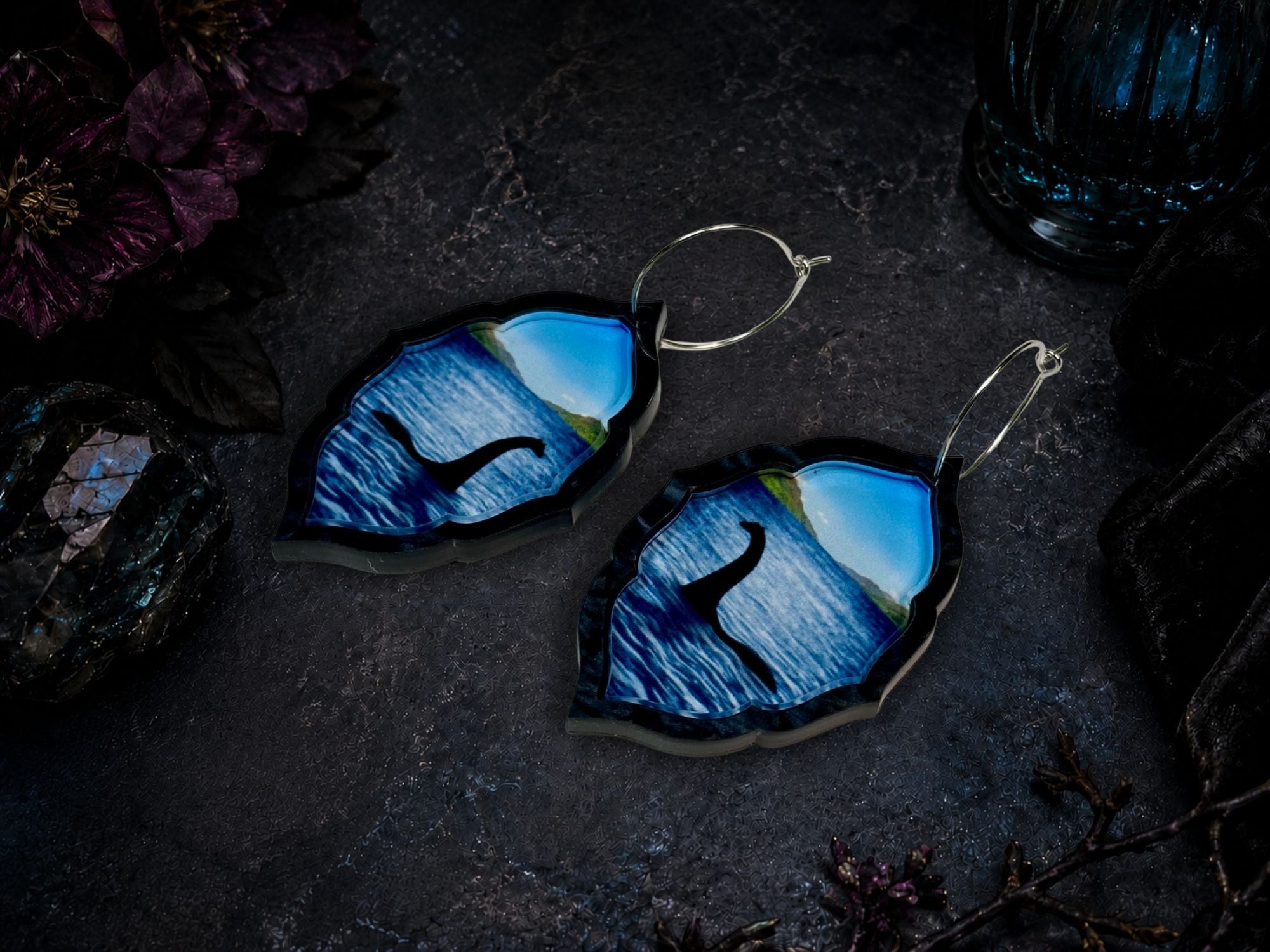 Acrylic Nessie earrings with blue water landscape photographed on dark moody background.