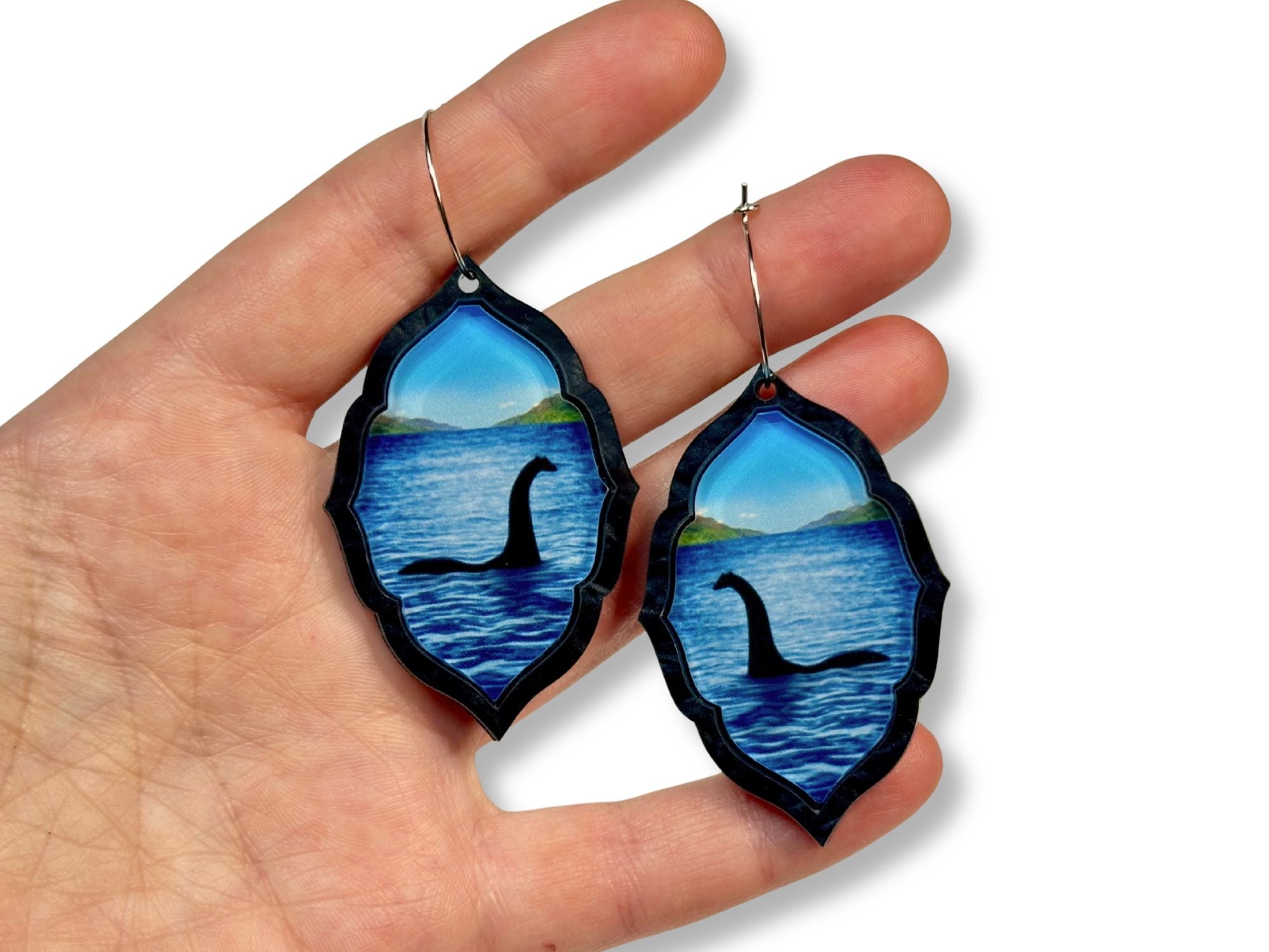 Hand holding blue lake monster acrylic earrings for size reference.