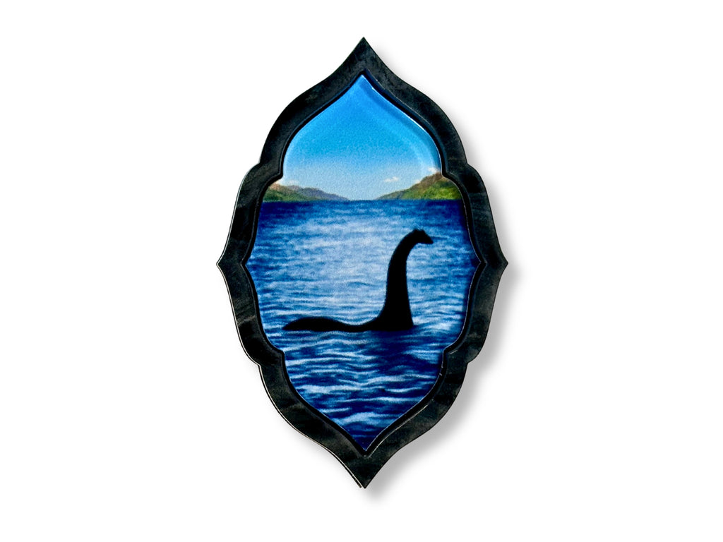 Original Loch Ness Monster brooch featuring blue lake artwork framed in black pearl acrylic.