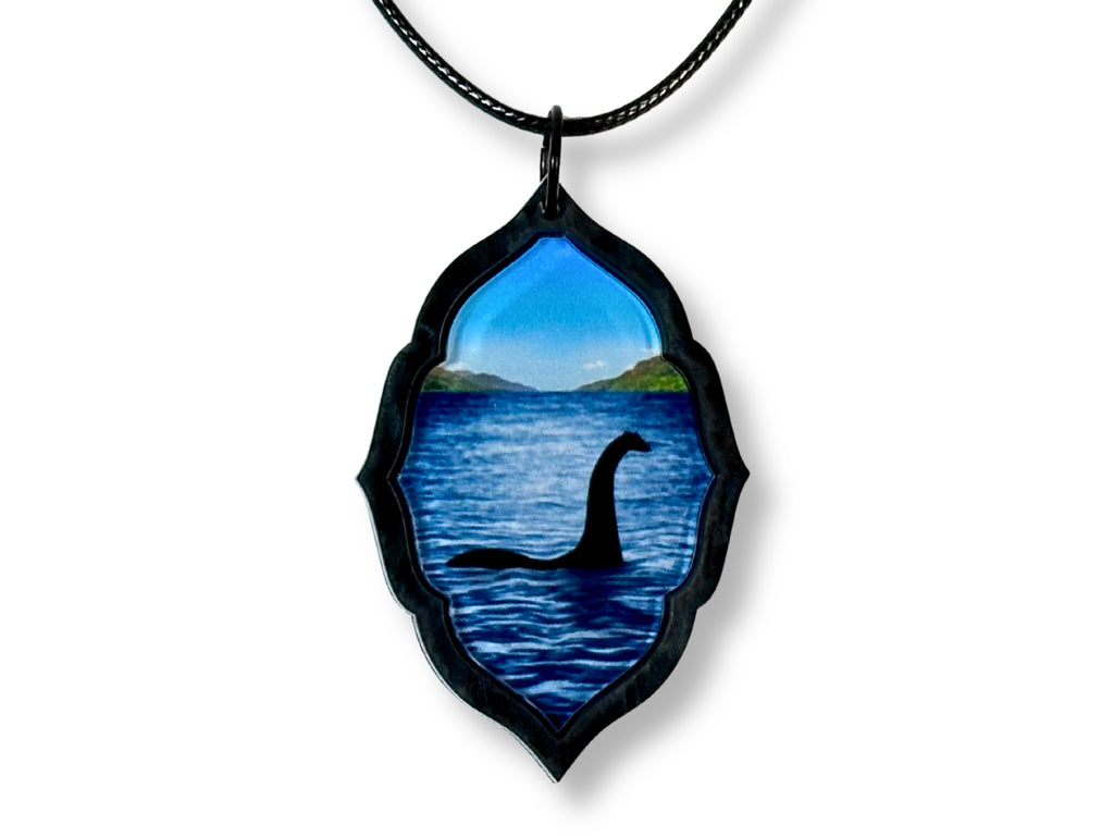 Loch Ness Monster acrylic pendant hanging from a black faux leather cord on a white background.