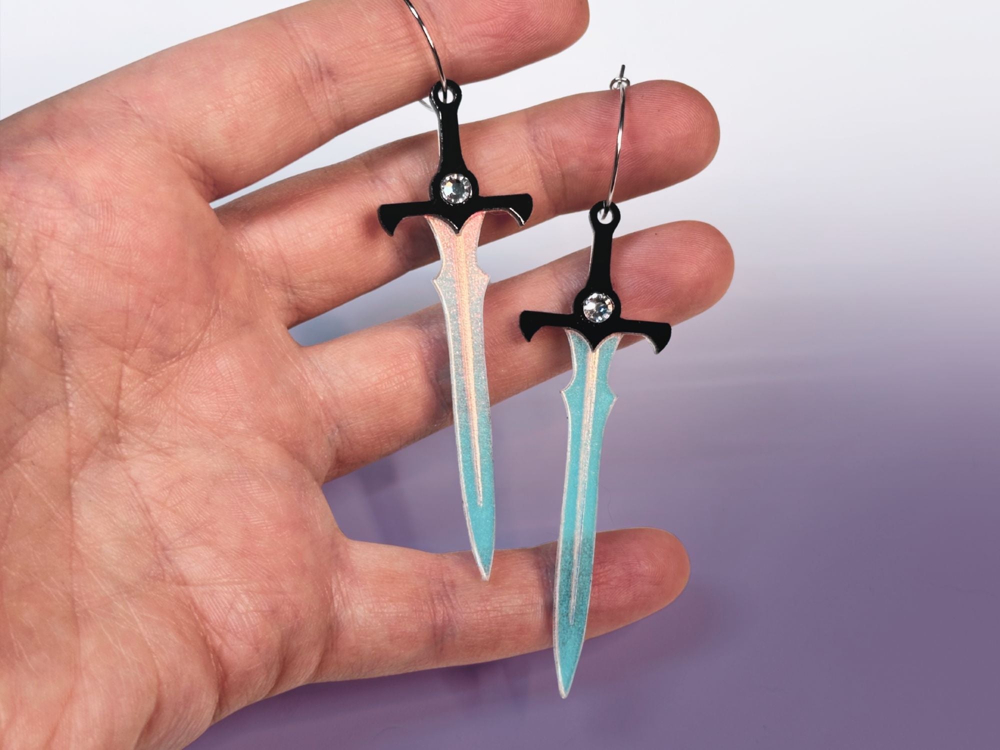 Hand holding sword earrings showing size and scale