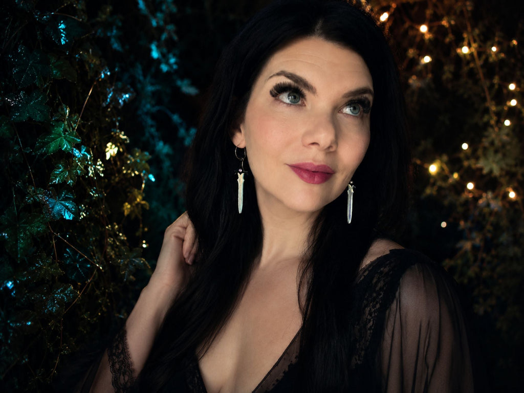 Woman wearing iridescent sword earrings with black jeweled hilts