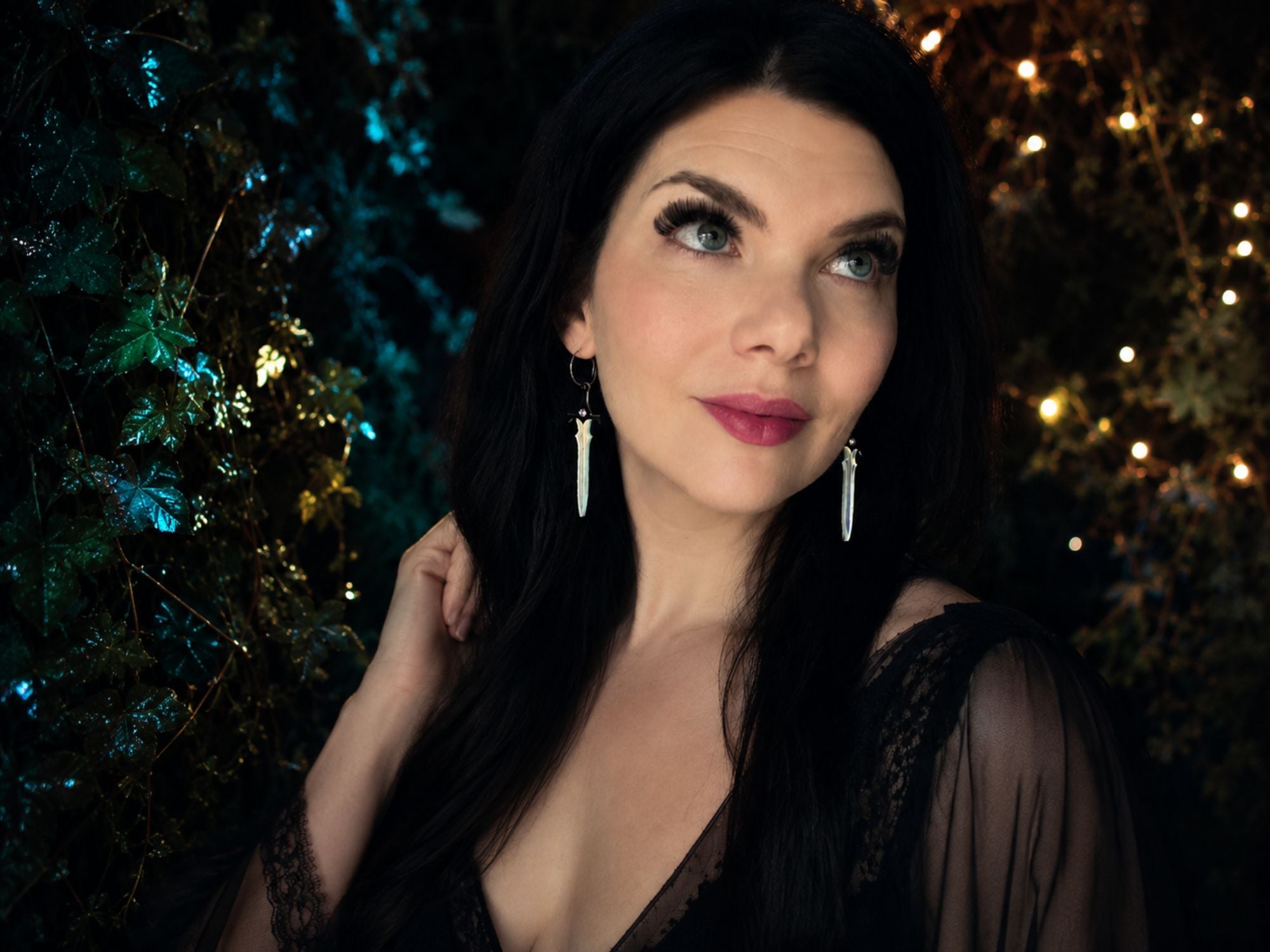 Woman wearing iridescent sword earrings with black jeweled hilts