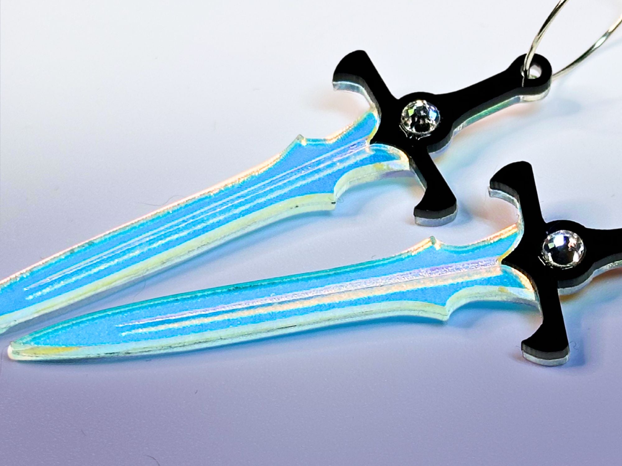 Close-up of engraved iridescent acrylic sword earrings with crystal accents