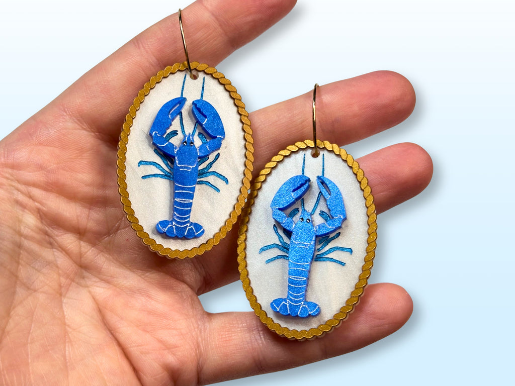 Blue lobster earrings held in hand showing statement size and layered design