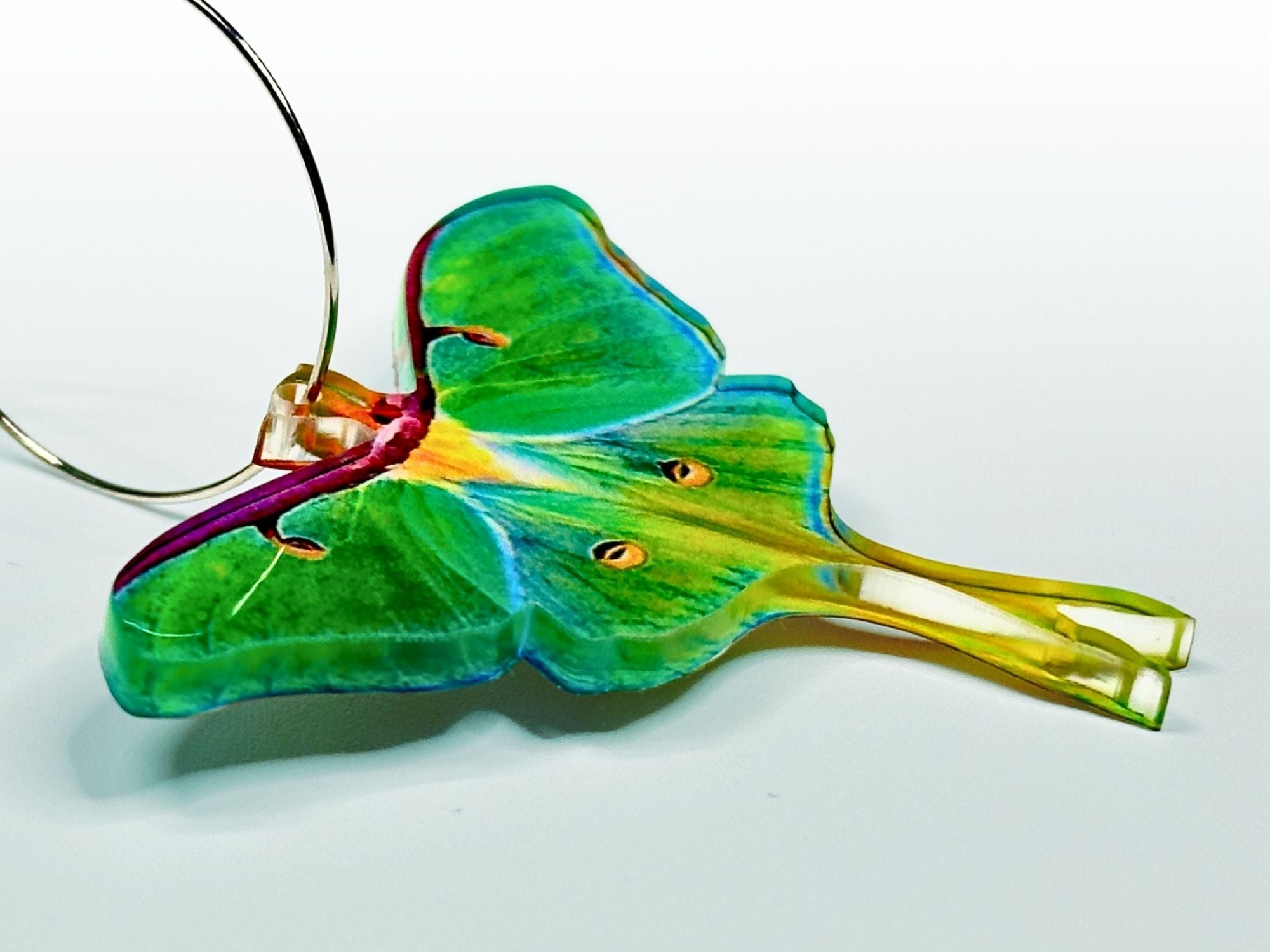 Side view of handmade sublimated vivid green luna moth earring with hoop showing thickness and translucency.